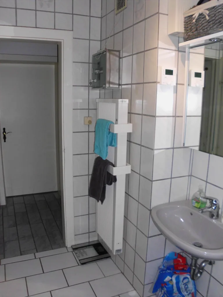 Schlanker weißer Badheizkörper mit Handtüchern in einem hellen Badezimmer