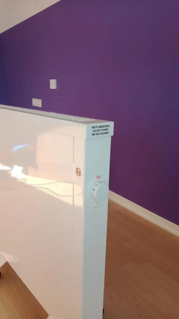 Nahaufnahme des Reglers einer Elektroheizung vor violetter Wand