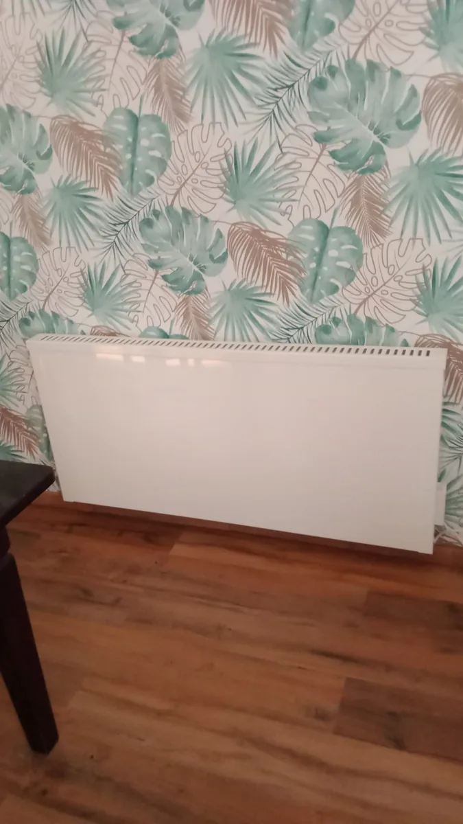 Weiße Elektroheizung in einem modernisierten Wohnraum vor einer Wand mit Blattmuster