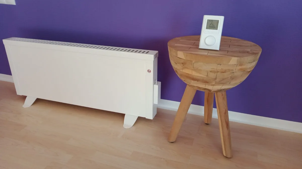 Weiße Elektroheizung mit digitalem Thermostat vor einer violetten Wand