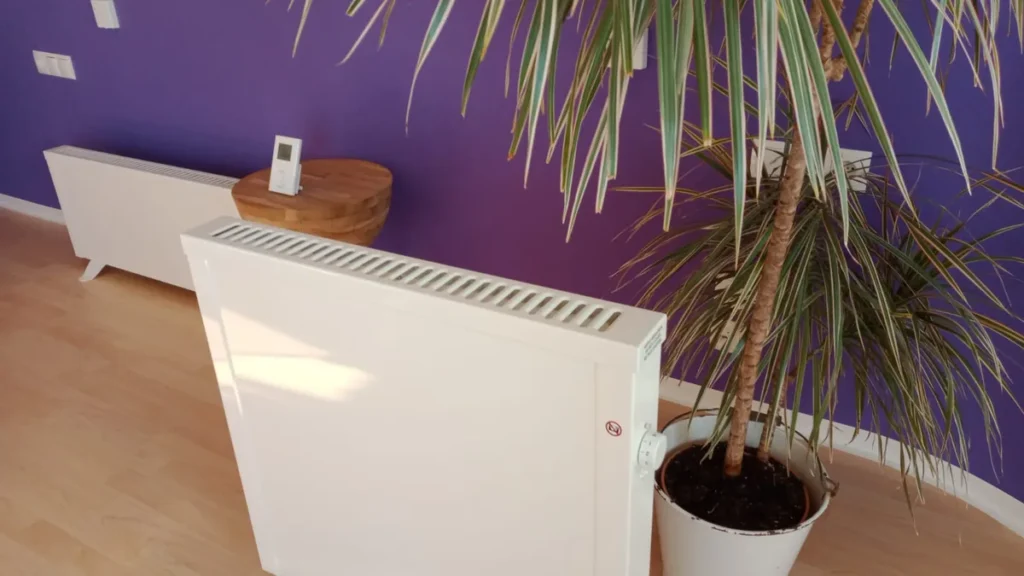 Elektroheizung mit digitalem Thermostat auf einem kleinen Hocker vor violetter Wand