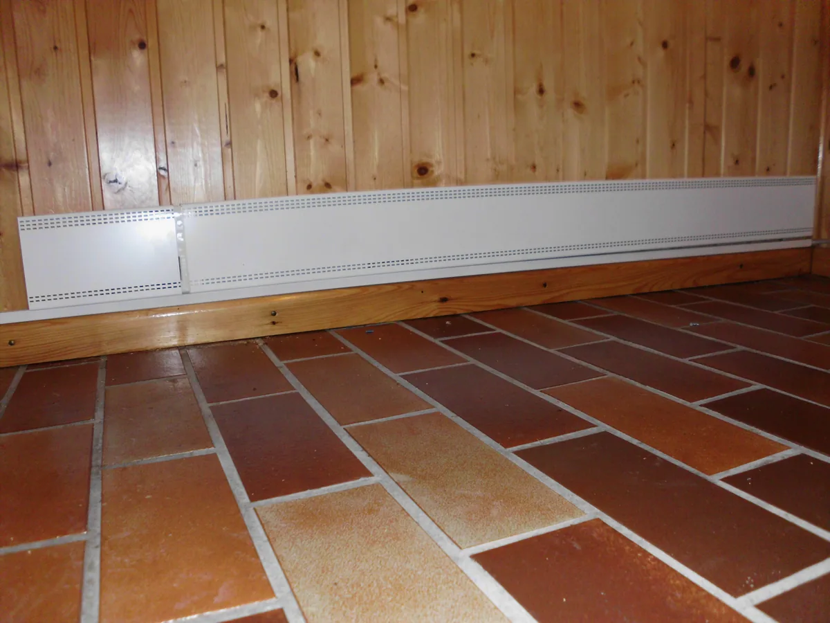 Weiße Fußleistenheizung vor einer Holzwand